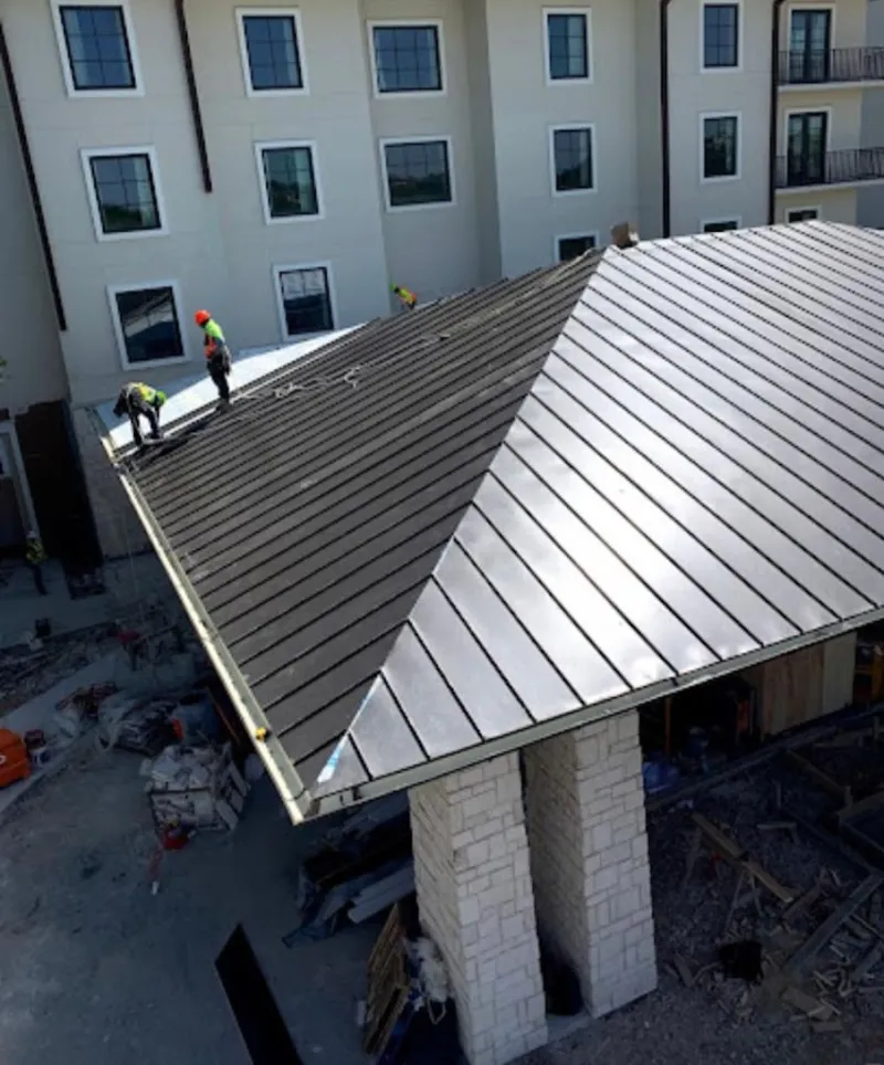 Crew installing standing seam metal roof panels on a commercial project in Boone